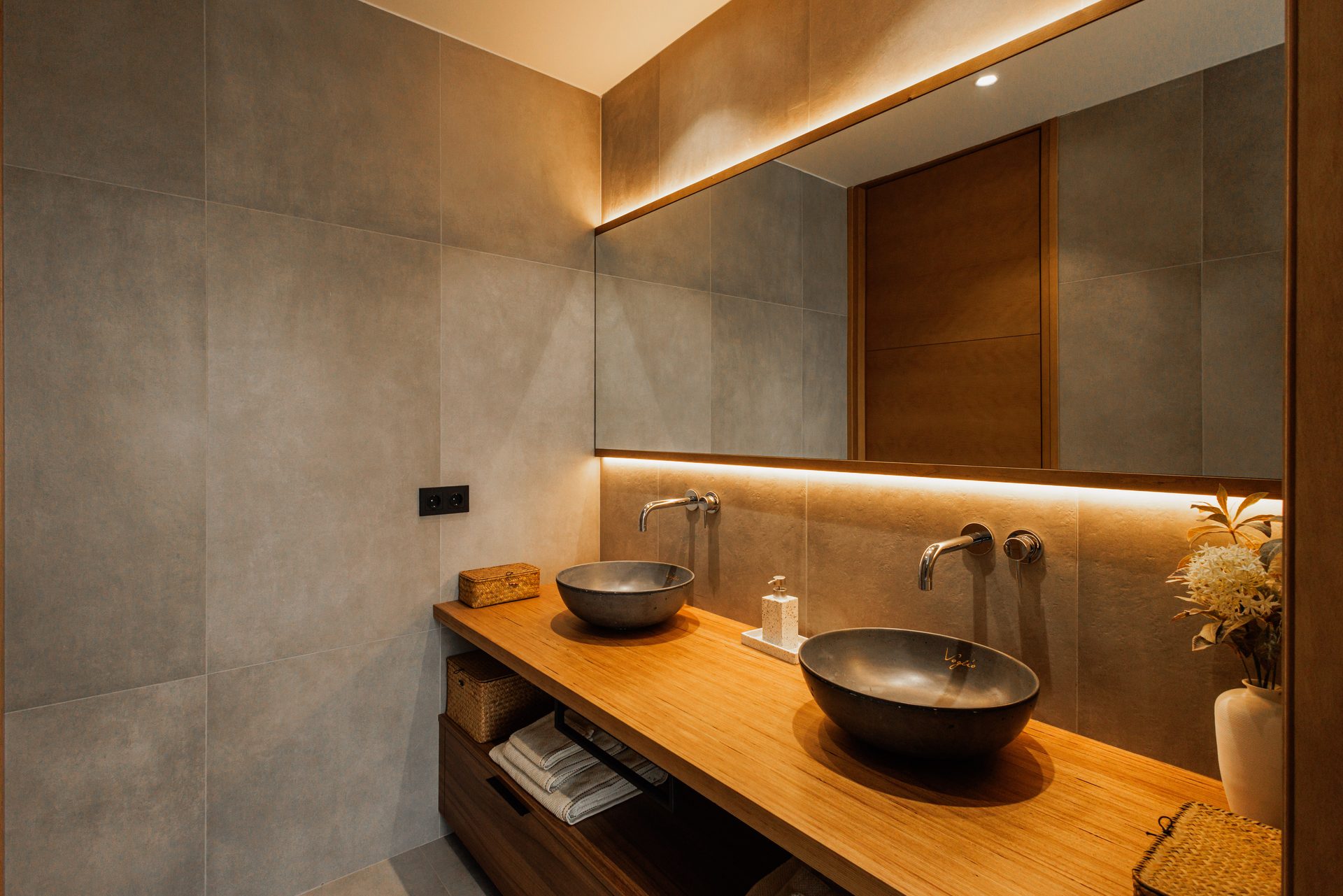 Baño de Villa Bali con lavabo de piedra sobre encimera de madera y luz lineal tras el espejo